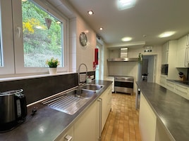 A modern kitchen with a stainless steel sink, a built-in oven, and a window with a view of greenery.