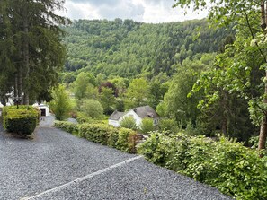 Ein Kiesweg führt zu einem Haus, umgeben von üppiger Vegetation und einem bewaldeten Hügel.