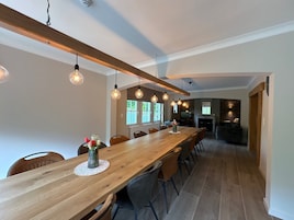 Un comedor con una larga mesa de madera, lámparas colgantes y vista a una sala de estar.