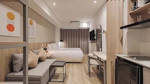 A compact hotel room with a bed, a sofa, a small table, a mirror, a TV, and a kitchenette. - Laureles Studio 303Q (Medellín)