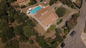 Luchtbeeld van een woonhuis met zwembad, schotels en een auto op straat.