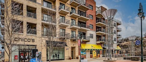 A multi-story building with balconies, a patio area with benches, and a storefront with a yellow awning.