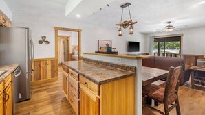 A modern kitchen with wooden cabinetry, a granite countertop island, and a dining area with a wooden table and chairs. - 4 Bears Lodge at Edgewater - Entire Lodge 6 Rooms (Forsyth)