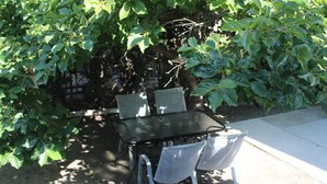 Una mesa y cuatro sillas en un espacio exterior sombreado, rodeado de abundante vegetación.