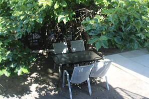 Ein Tisch und vier Stühle in einer schattigen Außenbereich mit dichtem Grün.