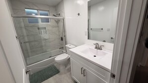 Un baño con ducha de vidrio, inodoro, lavabo con espejo y alfombra verde.