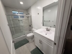 Ein Badezimmer mit Duschkabine, Toilette, Waschbecken mit Spiegel und einem grünen Teppich.
