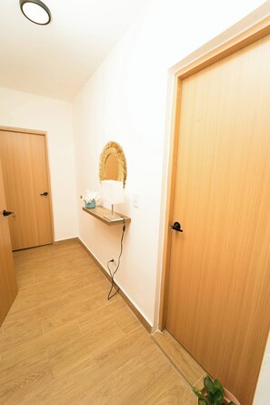 A hallway with wooden flooring, a door on the right, a wall-mounted shelf with a lamp, and a potted plant. - Perfect Place in Samana 1 (Samaná)