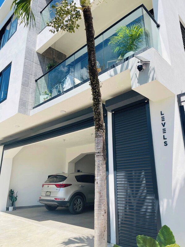 A modern building with a car parked in the garage, a palm tree, and a security camera. - Perfect Place in Samana 1 (Samaná)