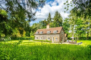 Ein Steinhaus mit Garten, einer Terrasse mit Gartenmöbeln und einem großen Baum im Hintergrund.
