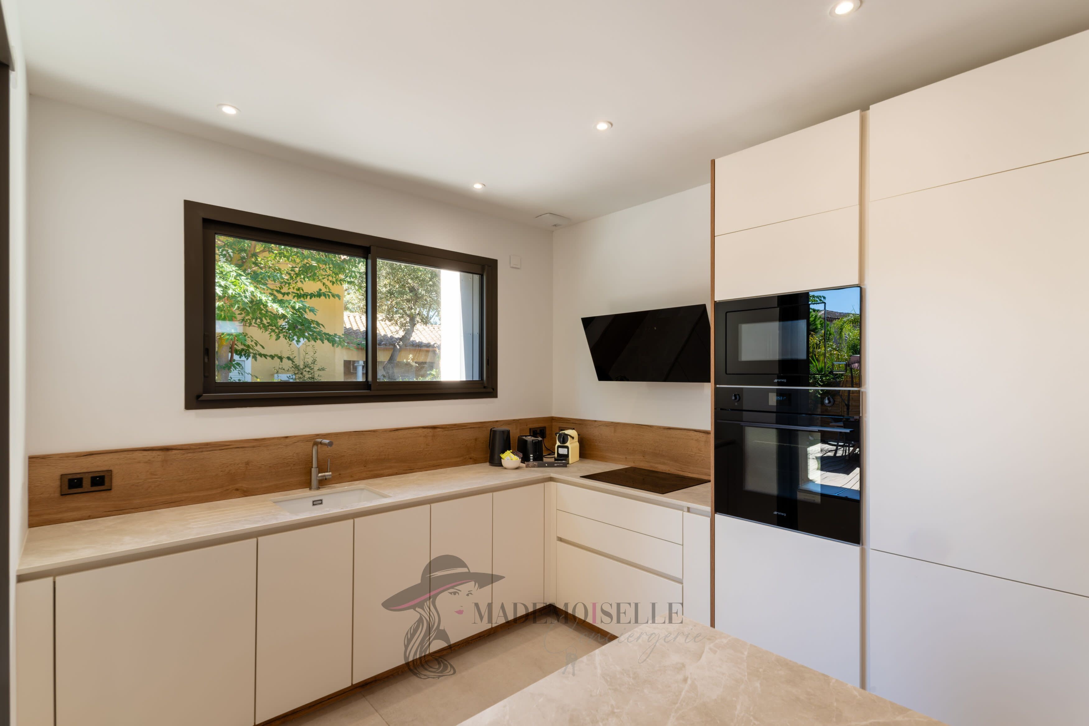 A modern kitchen with a built-in oven, microwave, and a window with a view of greenery.