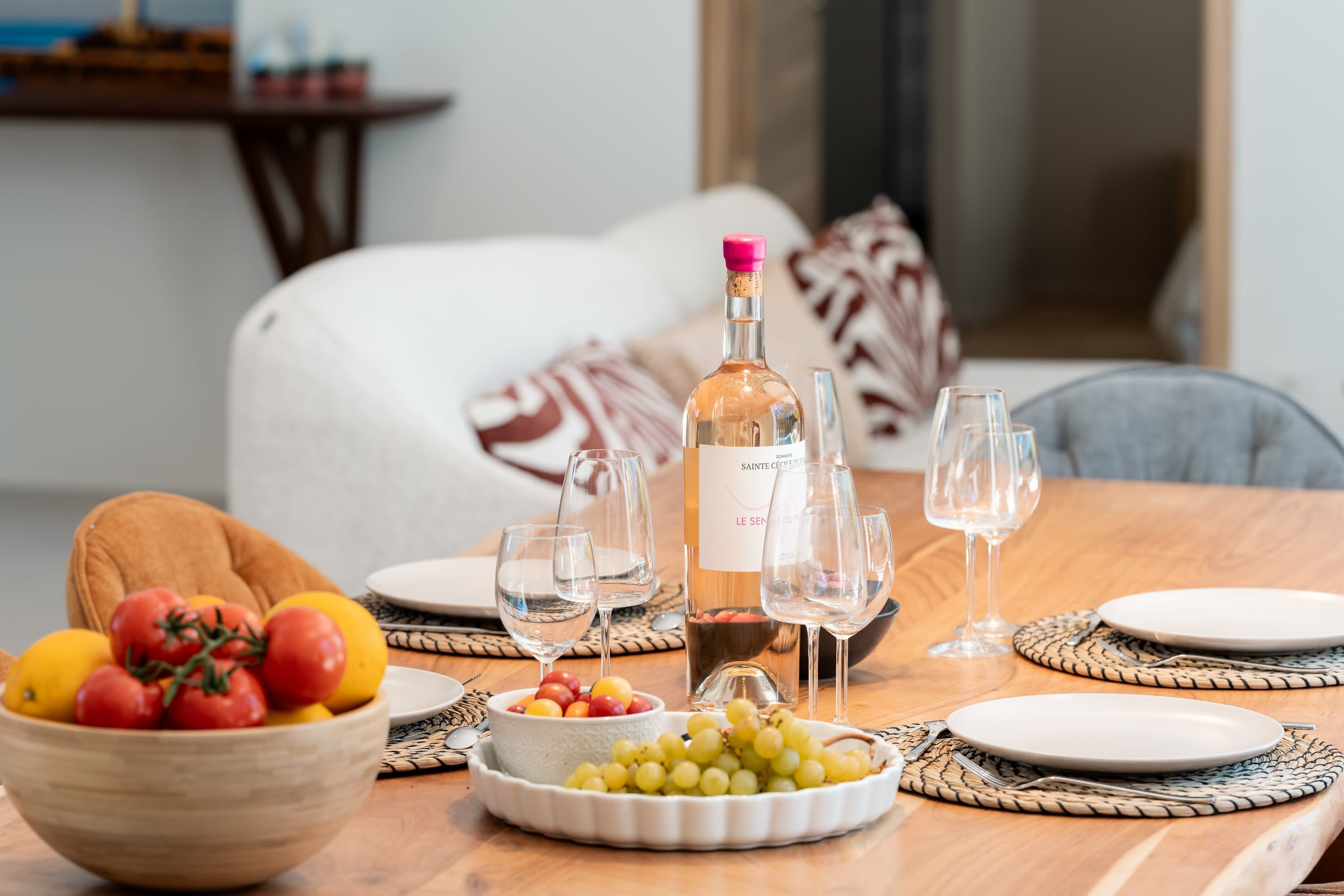 A dining table set with a bottle of wine, glasses, plates, and bowls of fruit and grapes.