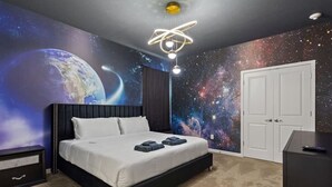 Ein Schlafzimmer mit Bett, Nachttisch, Kommode, Deckenleuchte und Wandgemälde von Weltraum.