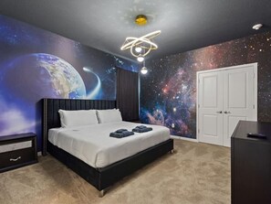 Ein Schlafzimmer mit Bett, Nachttisch, Kommode, Deckenleuchte und Wandgemälde von Weltraum.