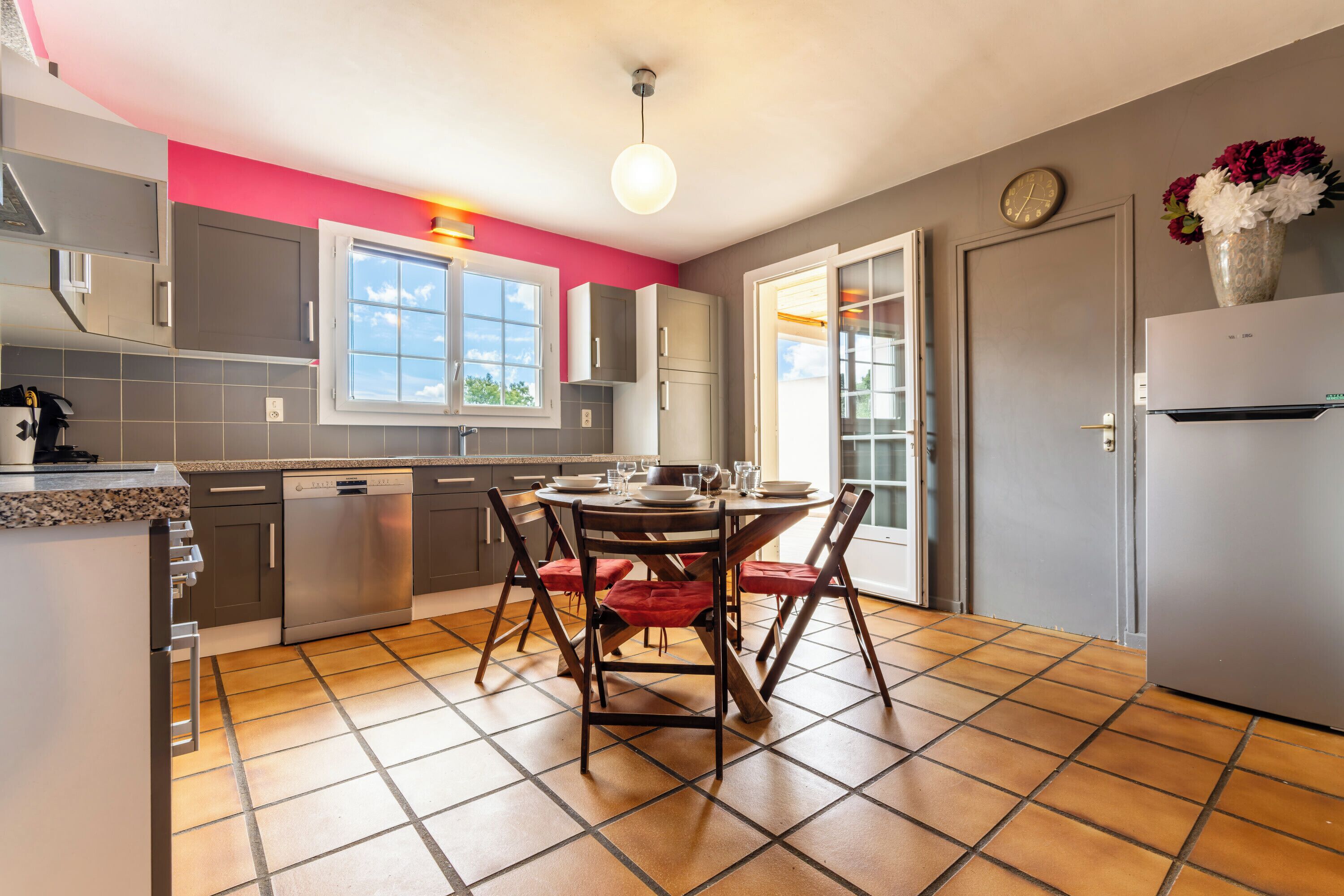 A modern kitchen with a dining table, chairs, and a clock on the wall.