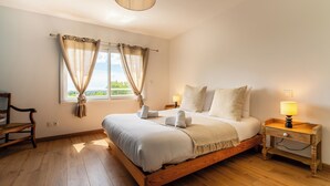 A bedroom with a wooden bed, a nightstand with a lamp, a chair, and a window with curtains.