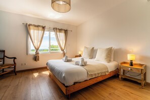 Ein Schlafzimmer mit einem Holzbett, einem Nachttisch mit Lampe, einem Sessel und einem Fenster mit Vorhängen.