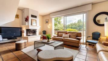 Een woonkamer met een televisie, bank, fauteuils en een open haard.