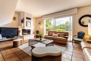 Ein Wohnzimmer mit Fernseher, Sofa, Sesseln und Kamin.