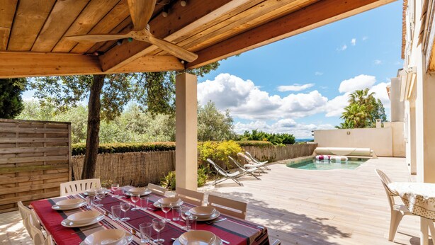 An outdoor dining area with a table set for six, a pool, and a covered patio.