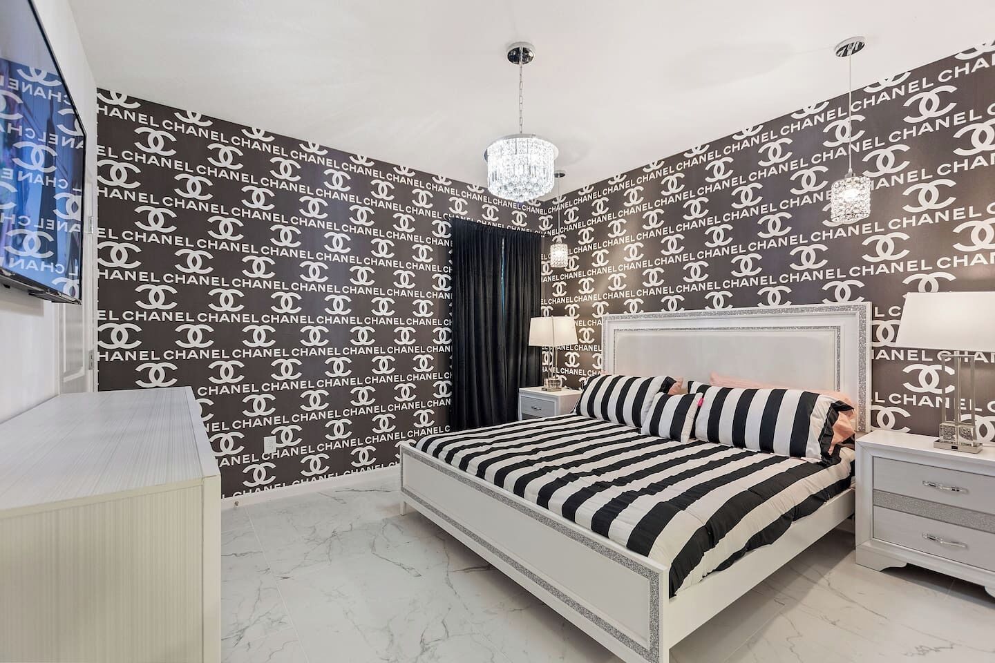 A bedroom with a bed, nightstands, a chandelier, and a TV.