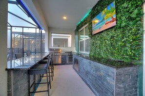 Eine moderne Küche mit einer Glasbar, einer grünen Wand mit Pflanzen und einem Gemälde über der Arbeitsplatte.