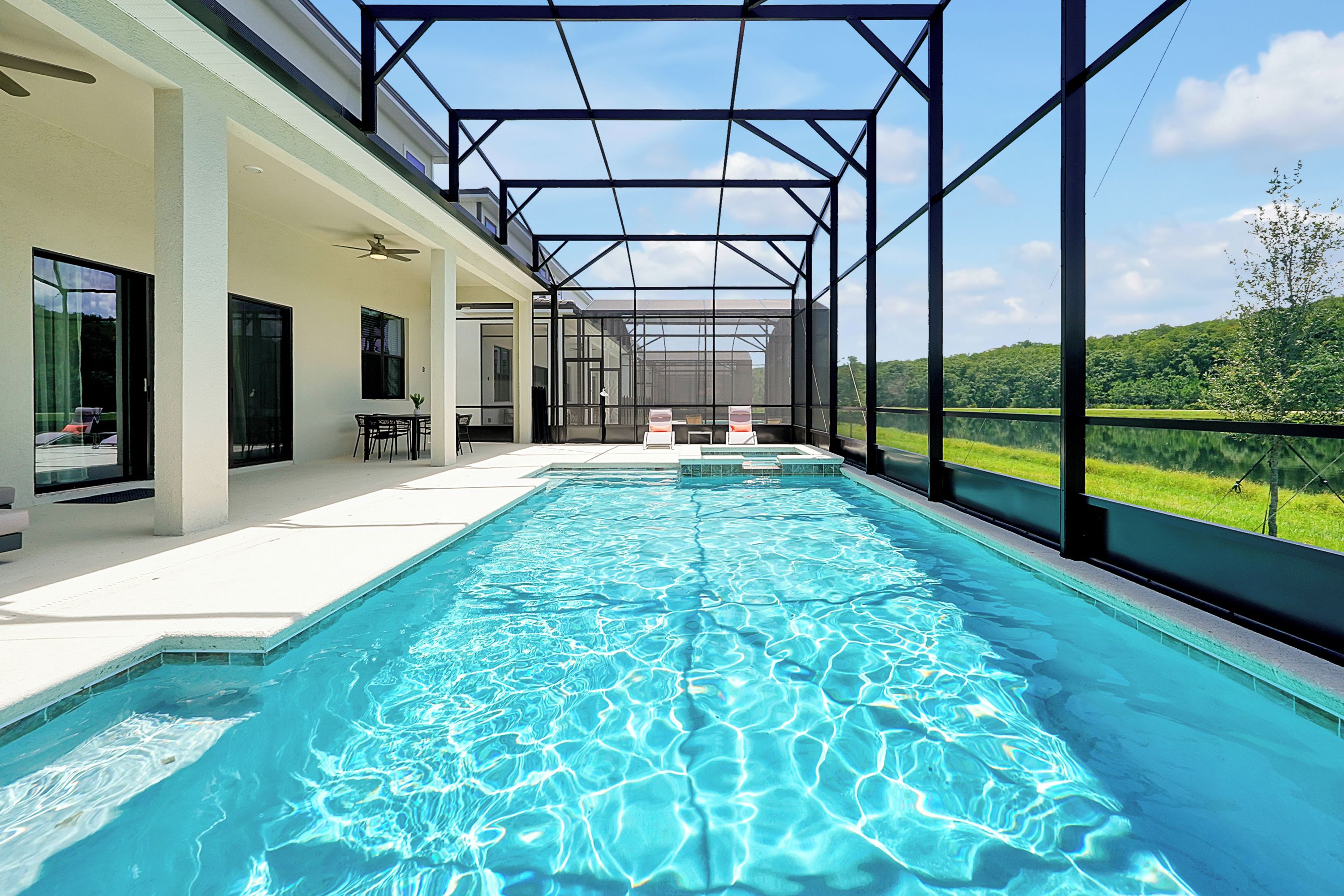 A swimming pool with a glass enclosure, a patio area with outdoor seating, and a view of a green landscape.