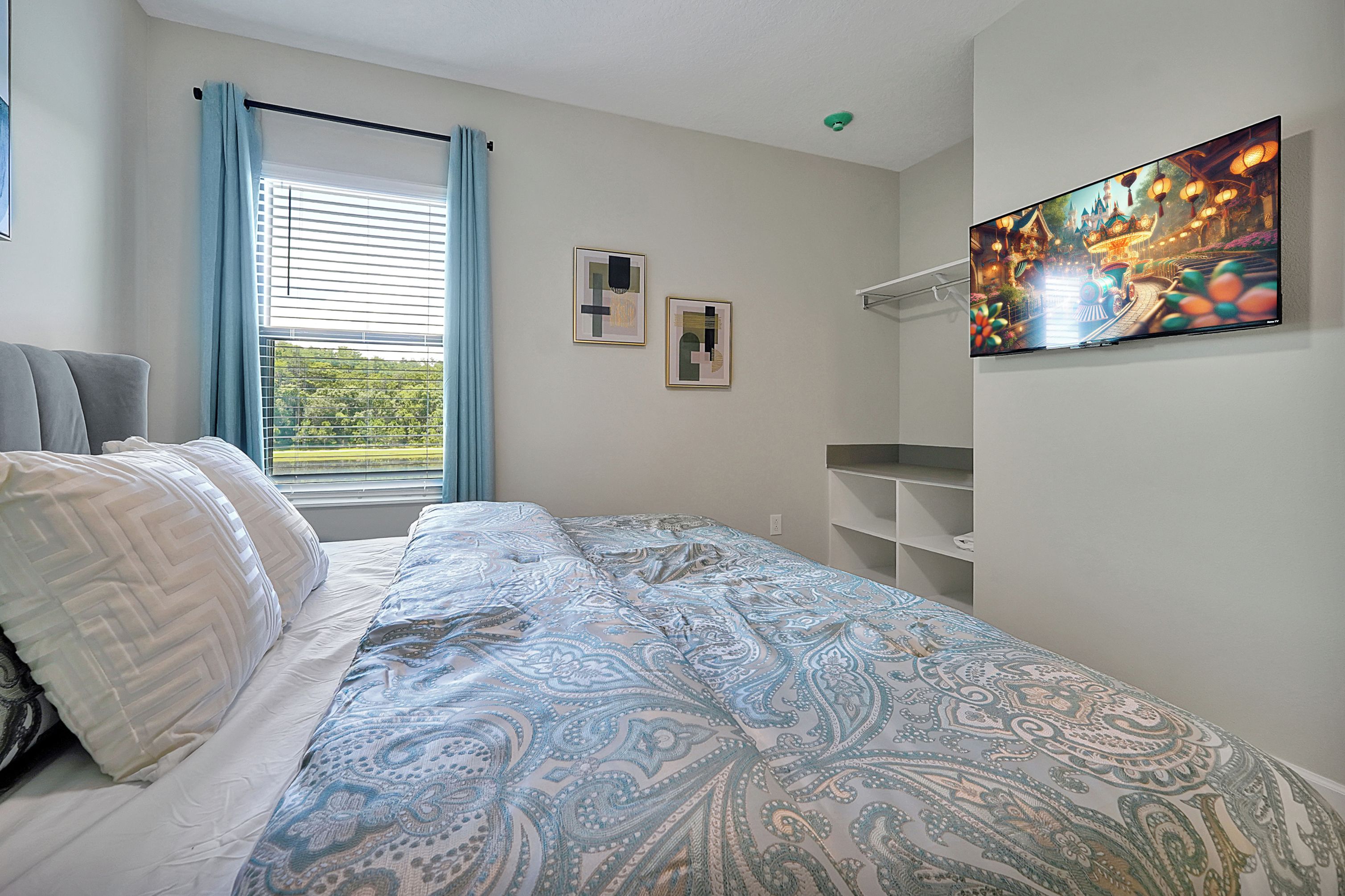 Een slaapkamer met een bed, een raam met gordijnen, een aan de muur bevestigde televisie en een plank.