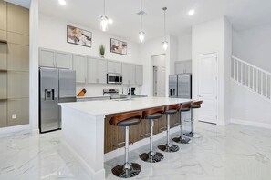 Eine moderne Küche mit weißen Schränken, Edelstahlgeräten, einer Marmorarbeitsplatte und einer Bar mit Barhocker.