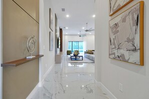 A hallway with a marble floor, a wooden shelf with a sculpture, and framed artwork on the walls. - Luxury Lake Views 15BR 16.5BA, Sleeps 40, Theater (Kissimmee)
