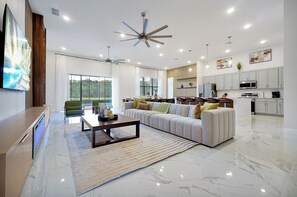 A spacious living room with a large sofa, a coffee table, and a television on a stand. - Luxury Lake Views 15BR 16.5BA, Sleeps 40, Theater (Kissimmee)