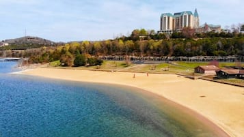 A coastal hotel with a beach, a large building with a green roof, and a hilly backdrop.