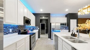 Een moderne keuken met witte kastjes, een blauwe betegelde achterwand, roestvrijstalen apparatuur en een centraal eiland met een spoelbak.