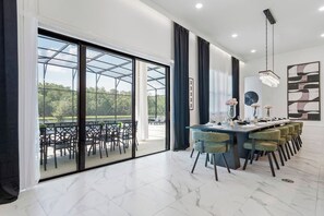 Ein moderner Essbereich mit einer verglasten Terrasse, einem langen Tisch mit Stühlen und einem Kronleuchter.