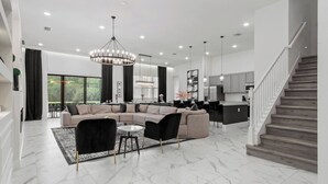 A spacious living area with a large L-shaped sectional sofa, a round coffee table, and a chandelier. - Regal 15BR 16.5BA, Sleeps 40, Lake View, Theater (Kissimmee)
