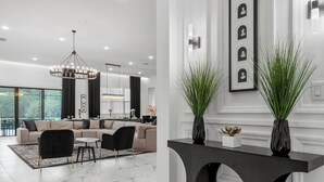 A modern living room with a sofa, chairs, a chandelier, and a dining area. - Regal 15BR 16.5BA, Sleeps 40, Lake View, Theater (Kissimmee)