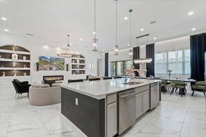 A modern kitchen with a large island, built-in shelving, and pendant lighting. - Regal 15BR 16.5BA, Sleeps 40, Lake View, Theater (Kissimmee)