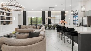 A modern living room with a sofa, dining area, and kitchen. - Regal 15BR 16.5BA, Sleeps 40, Lake View, Theater (Kissimmee)
