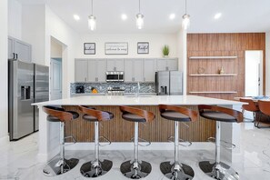 Eine moderne Küche mit Kochinsel, Barhocker, Edelstahlgeräten und einer Wand mit Holzverkleidung.