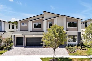 Ein modernes, zweistöckiges Haus mit Garage, Auffahrt und einem kleinen Baum im Vorgarten.