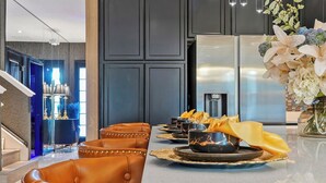 A modern kitchen with a stainless steel refrigerator, a dining area with leather chairs, and a decorative vase with flowers. - Stunning 12BR 11.5BA, Sleeps 27, Theater, Game Rm (Kissimmee)
