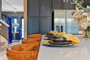 A modern kitchen with a stainless steel refrigerator, a dining area with leather chairs, and a decorative vase with flowers. - Stunning 12BR 11.5BA, Sleeps 27, Theater, Game Rm (Kissimmee)