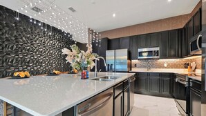 A modern kitchen with a large island, stainless steel appliances, dark cabinetry, and a decorative wall. - Stunning 12BR 11.5BA, Sleeps 27, Theater, Game Rm (Kissimmee)