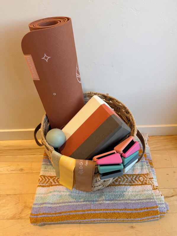 Un panier contenant un tapis de yoga, un autre panier en osier et un tapis à rayures, le tout posé sur un plancher en bois.