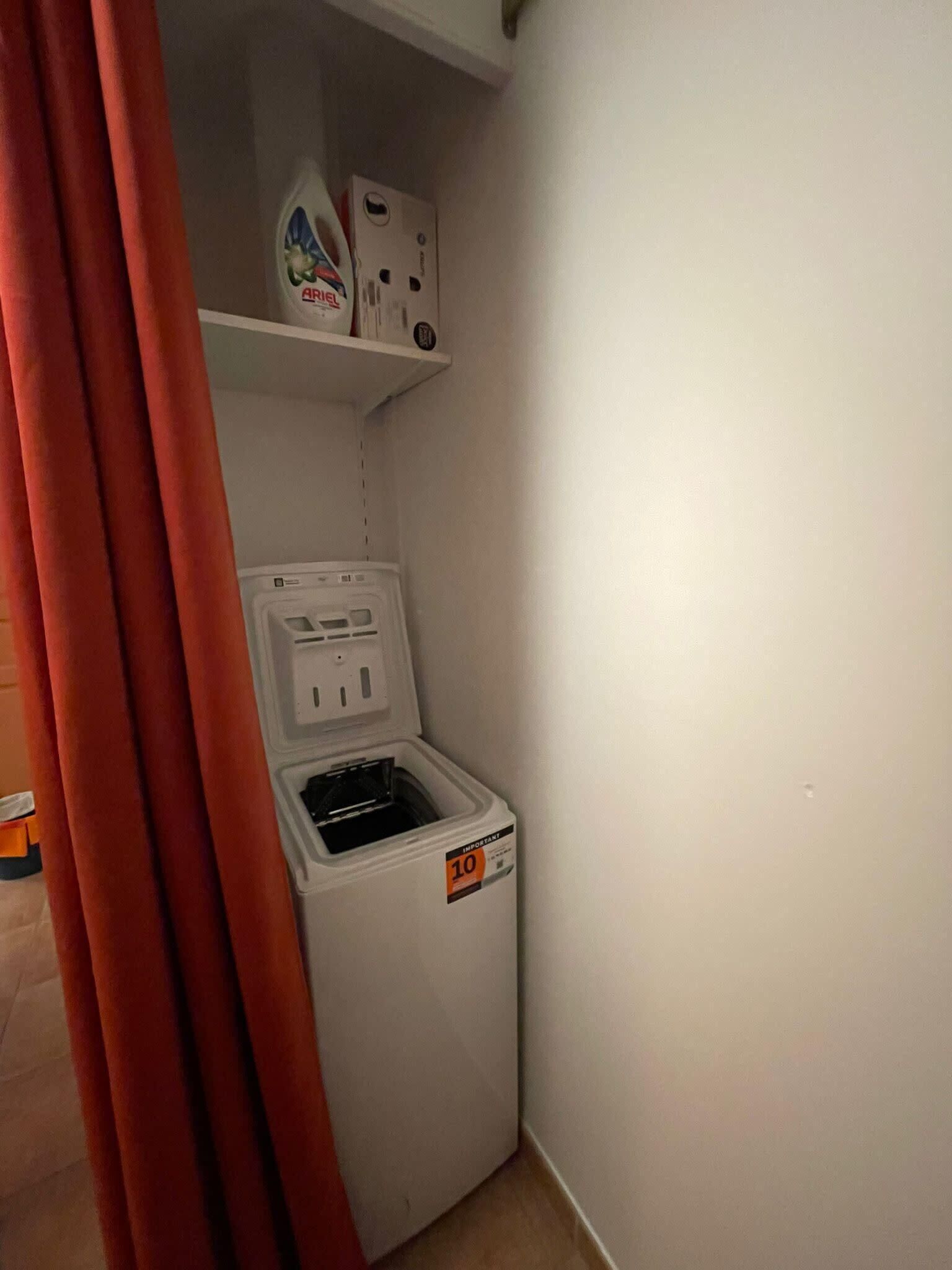 Un cuarto de lavado con lavadora, un estante con detergente y un enchufe.