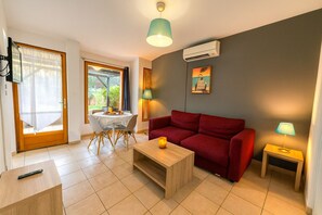 Ein Wohnzimmer mit rotem Sofa, einem Holztisch, einem Fernseher, einem Esstisch mit Stühlen und einem Fenster mit Vorhängen.
