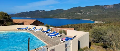 Un espace piscine avec des chaises longues bleues, une vue dégagée sur un lac et un paysage montagneux en arrière-plan.