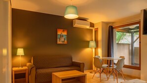 Een woonkamer met een bank, een salontafel, een eettafel met stoelen, een televisie en een schilderij aan de muur.