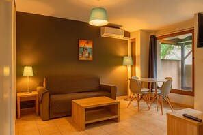Ein Wohnzimmer mit einer Couch, einem Couchtisch, einem Esstisch mit Stühlen, einem Fernseher und einem Bild an der Wand.