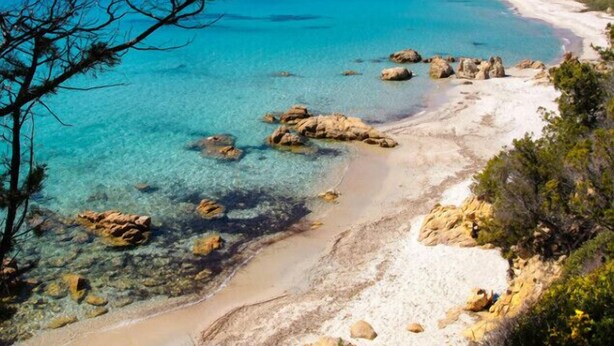 Een kustlandschap met helder turquoise water, rotsformaties en een zandstrand.